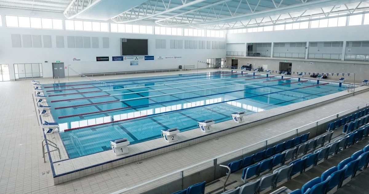 Pusty basen olimpijski z równymi torami i spokojną taflą wody, widok z trybun w jasnym świetle.