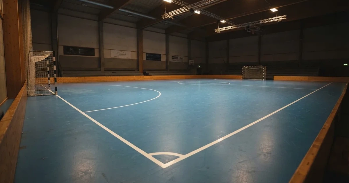Hala z niebieskim parkietem i niewielkimi bramkami po obu stronach, pusta, światło padające z sufitu.