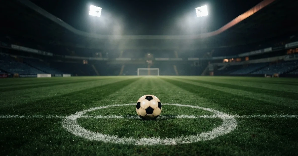 Piłka nożna leży na środku murawy pod rozświetlonym nocnym niebem, nad stadionem unosi się lekka mgła, a trybuny toną w półmroku.