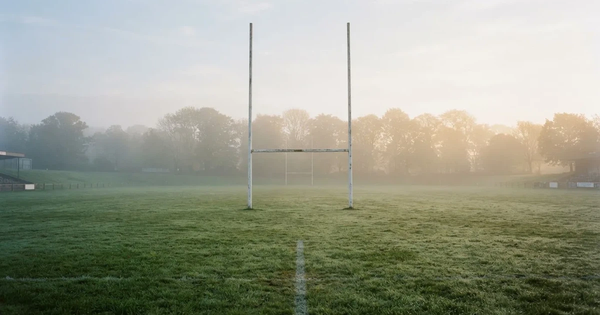 Bramka do rugby w kształcie litery H stoi na pustym boisku w mglisty poranek, w tle linia drzew.