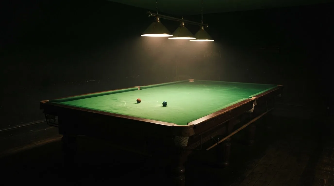 Lampa nad stołem rzuca stożek światła na zielone sukno, reszta pustego pokoju tonie w mroku.